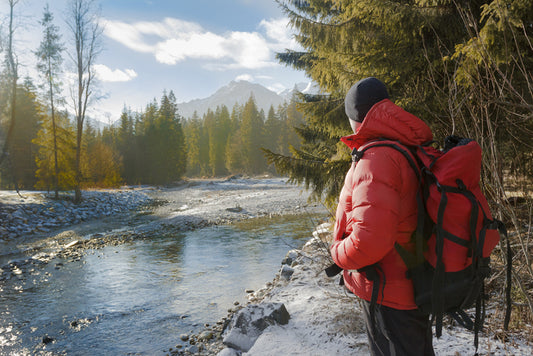 man in red down jacket by river and mountains